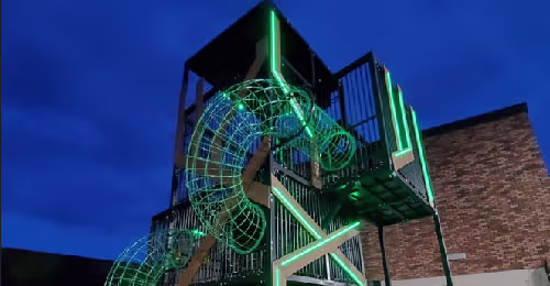 Alsuper: A three-level illuminated tower featuring climbing, rope walkways and slides inside a retail environment.